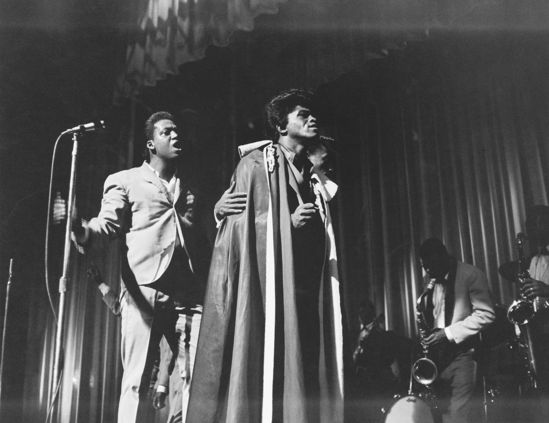 James Brown in his famous cape, helped offstage by MC Danny Ray at the Apollo Theater, 1964. Photo via Michael Ochs Archives/Getty Images.